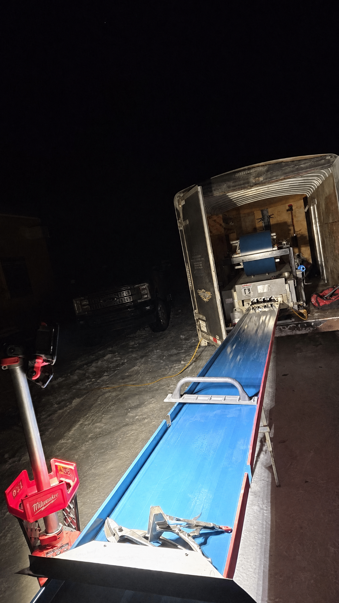 A long blue pre-finished metal panel exiting the mobile roll-former at night on a snowy Saskatchewan jobsite