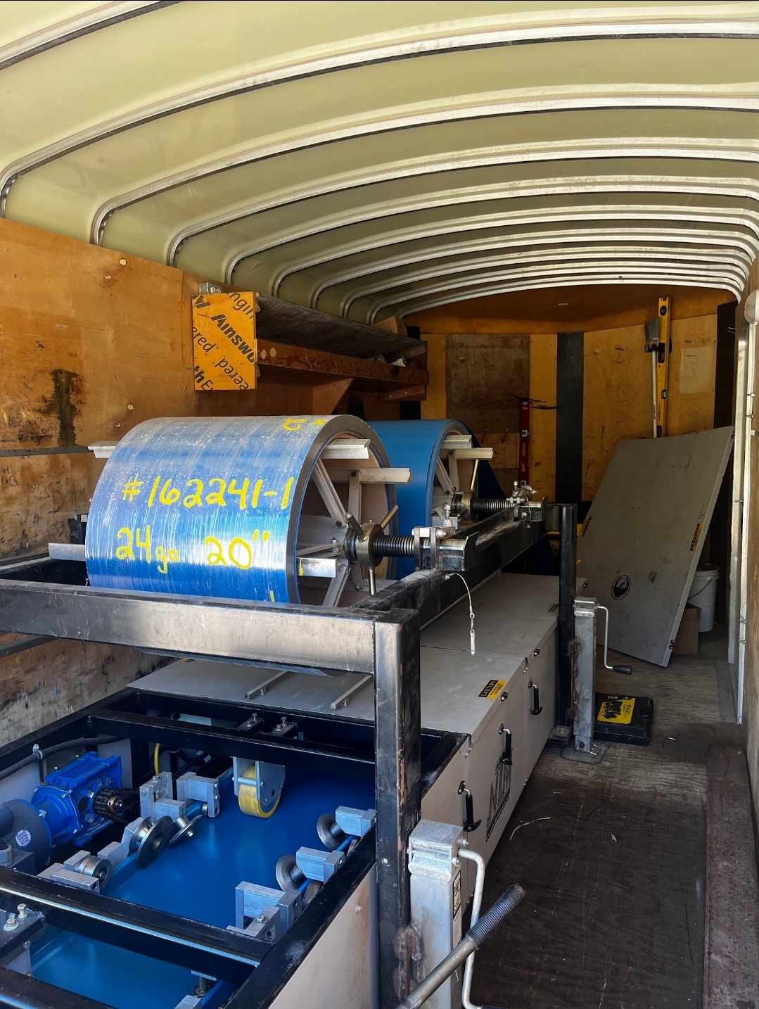 Inside the Sask Seamless mobile trailer showing a labelled 24-gauge 20-inch steel coil mounted on the roll-former mandrel