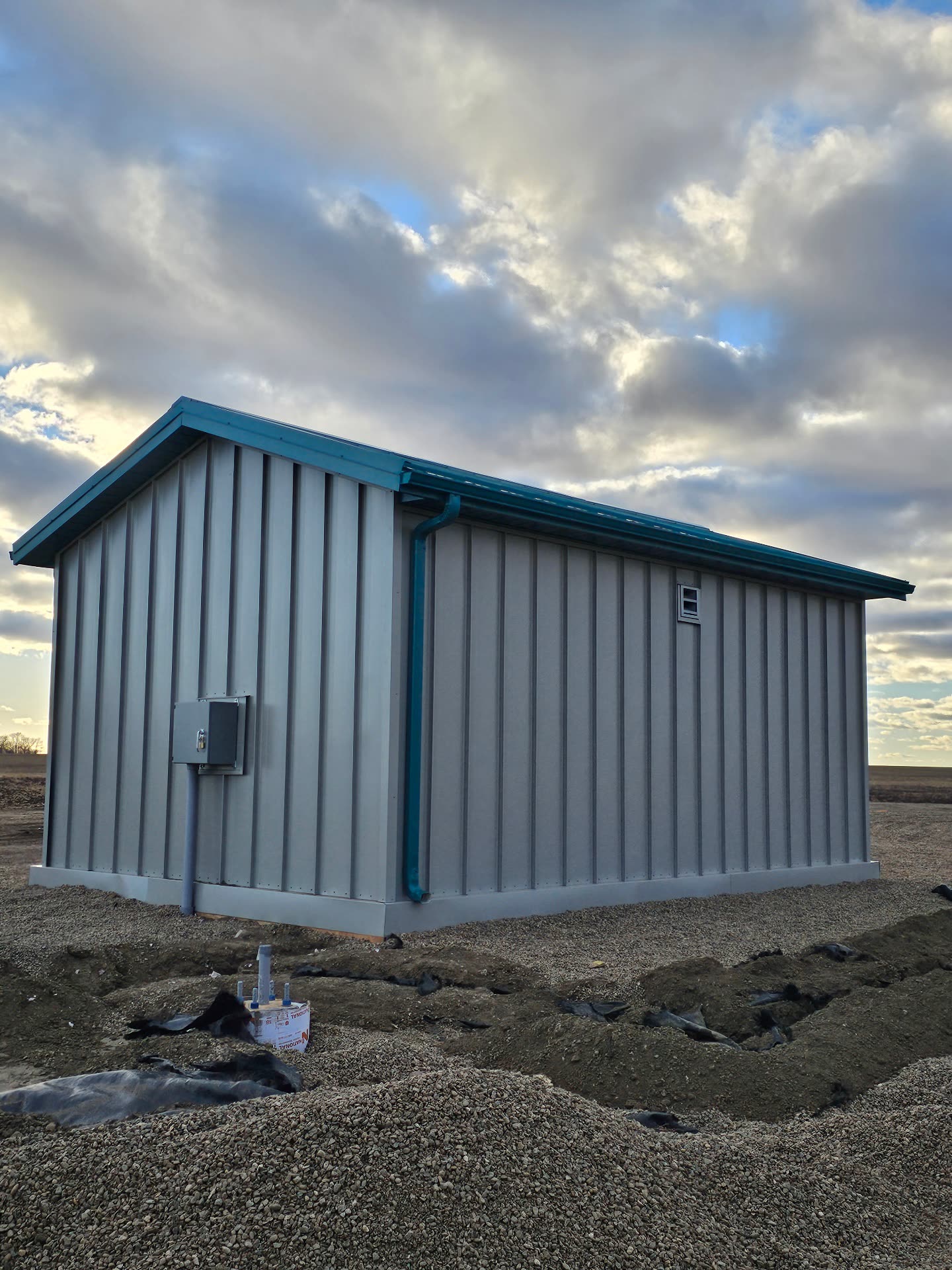 Side elevation — stone grey metal siding with green seamless eavestrough and downspout.